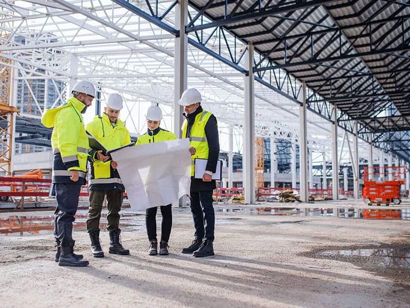 Group of engineers with blueprints standing on construction site. Front view of group of engineers with blueprints standing on construction site.